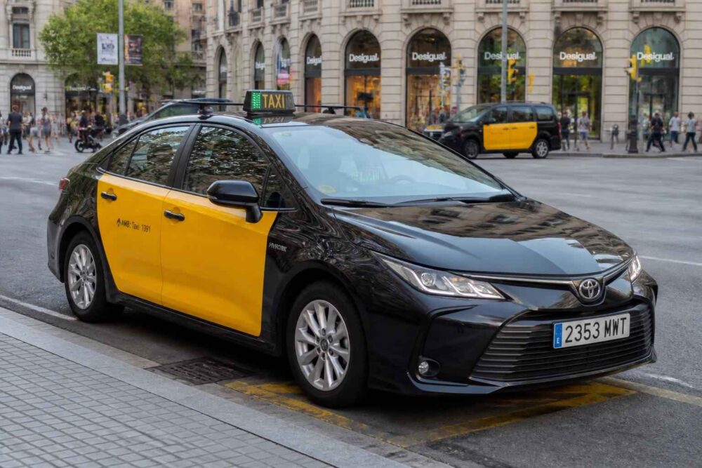 Czarno-żółta Toyota z oznaczeniem taxi zaparkowana przy ruchliwej ulicy w centrum miasta